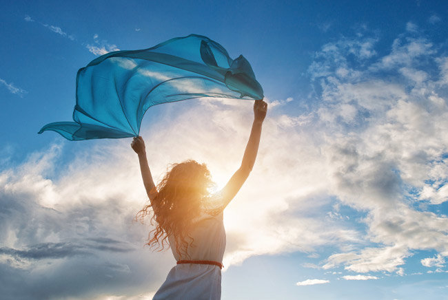 Femme avec un foulard dans le vent sous un ciel nuageux ensoleillé